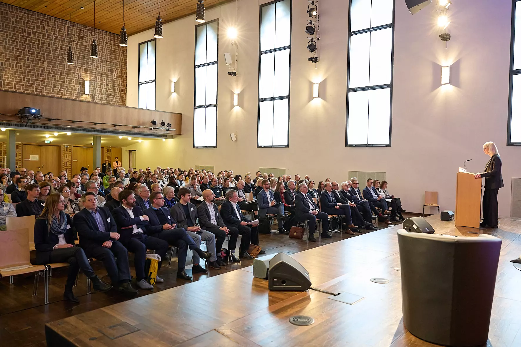 Arbeitsministerin Ulrike Scharf steht an einem Rednerpult. Vor ihr ist ein bestuhlter Saal voller Menschen zu sehen.